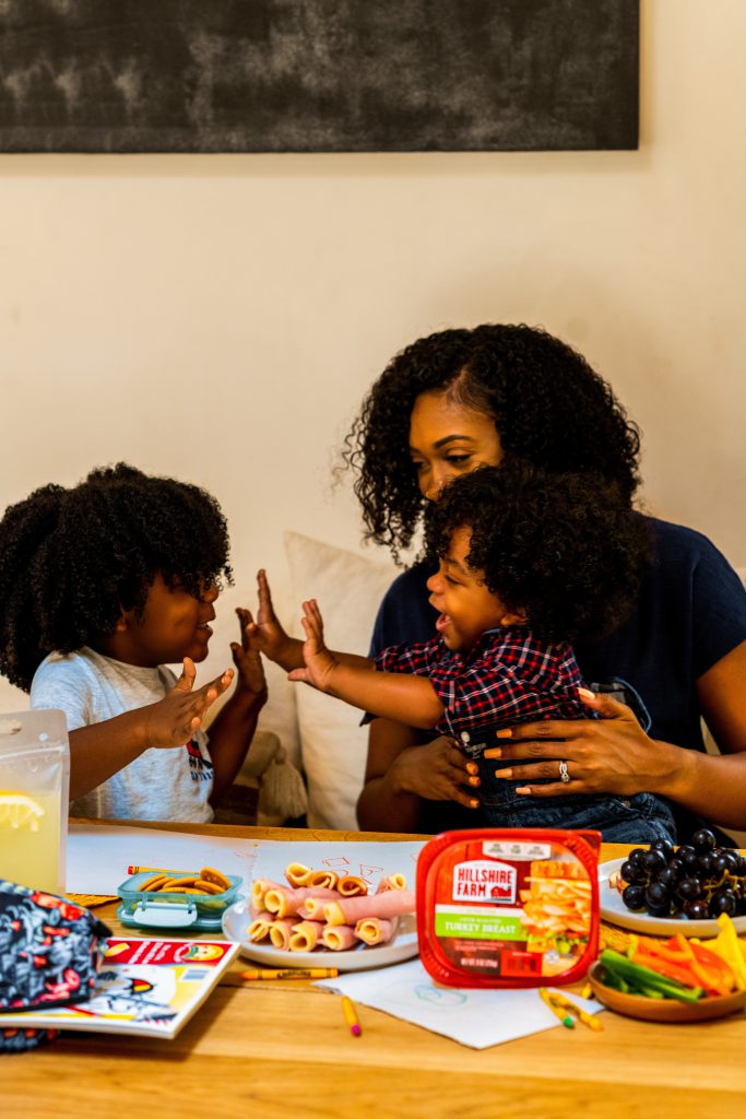 A happy mother plays with her two children, she holds one that reaches out to their sibling.