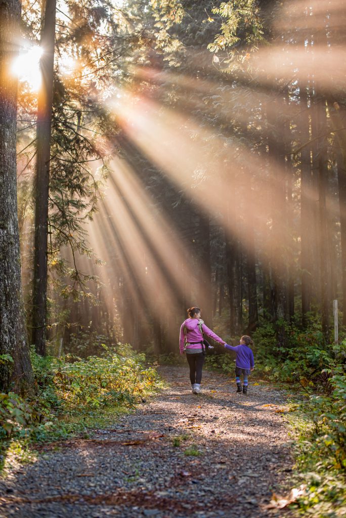 A mother walks with her child outside on a park trail.