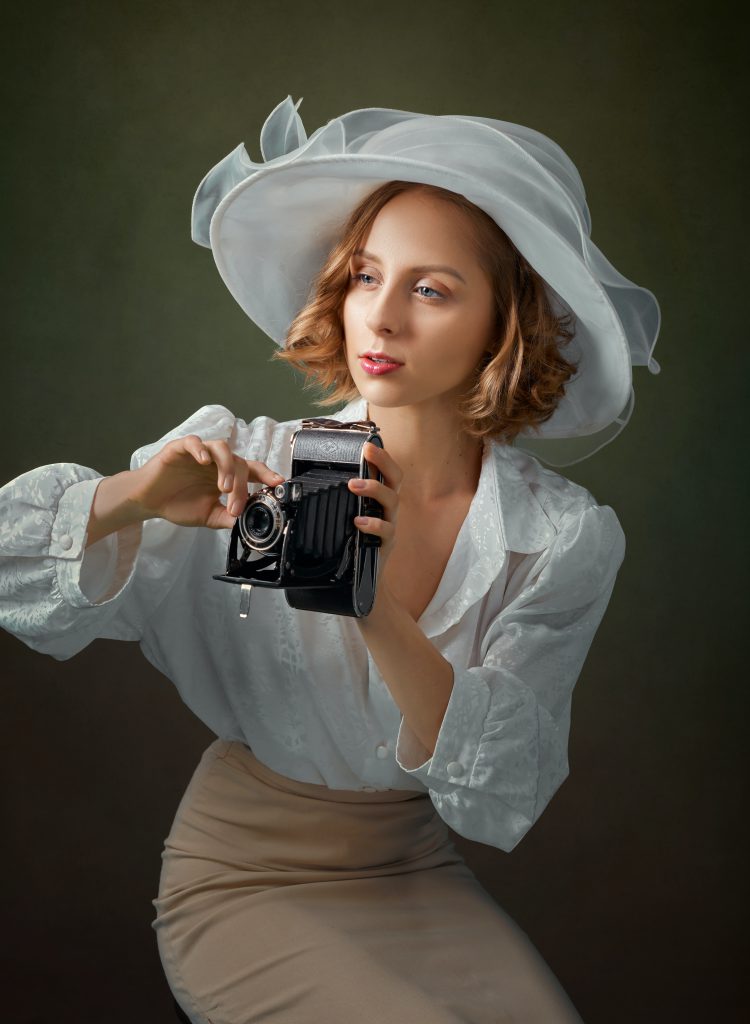 Beautiful woman who peers out of frame while holding a camera. She wears white Kentucky Derby Churchill Downs styled hat.